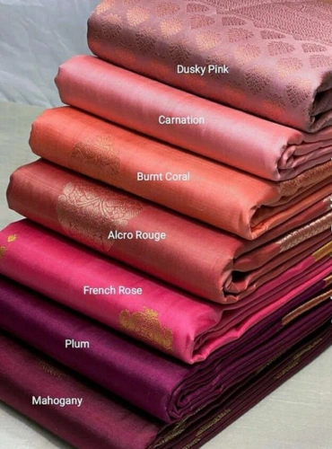 Stacked silk sarees in elegant shades of dusky pink, carnation, burnt coral, alaro rouge, french rose, plum, and mahogany displayed in a boutique showroom.